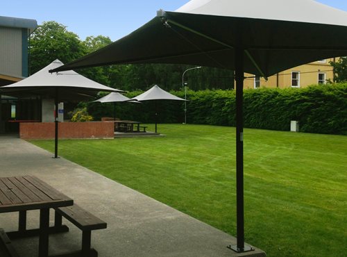 Parasol Umbrella placed around the rim of an outside dining area next to a grass field